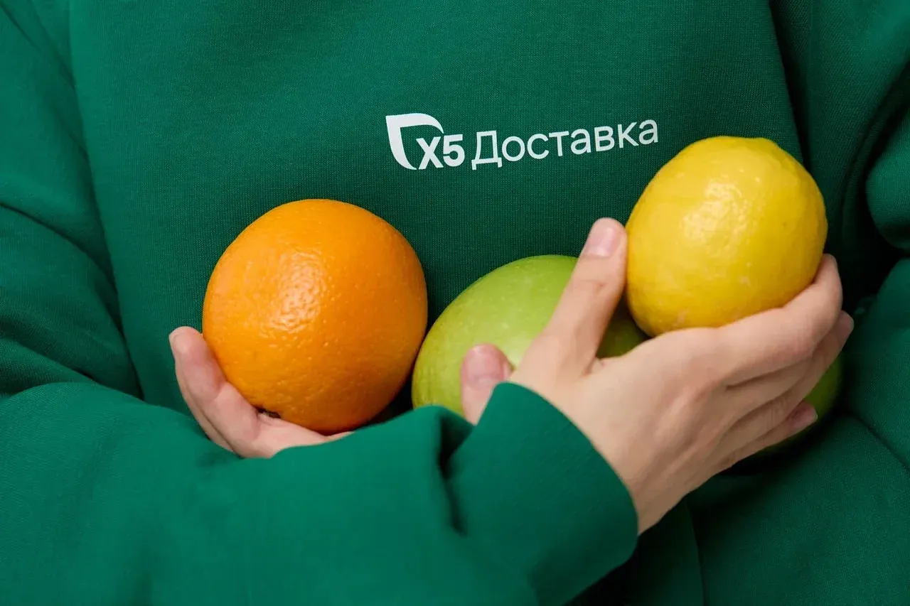 сборщик из x5 Доставка держит в руках лимон, апельсин и яблоко